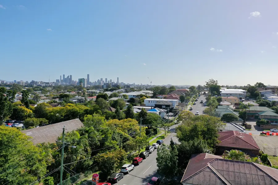 Drone photo above the site: tree-lined streets of Greenslopes with the Brisbane CBD skyline on the horizon